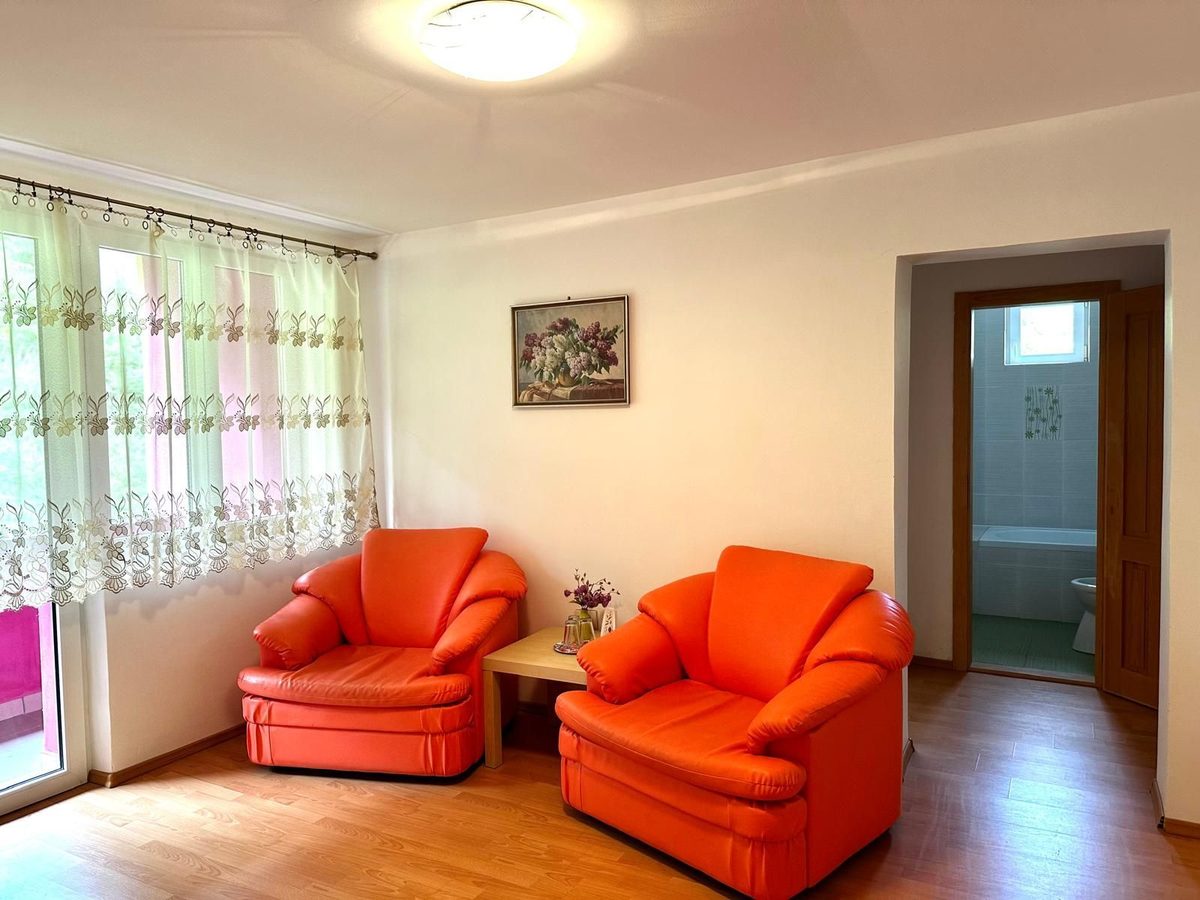 Colțul de zi al unui apartament, cu două fotolii portocalii lângă fereastră și ușa deschisă spre baie