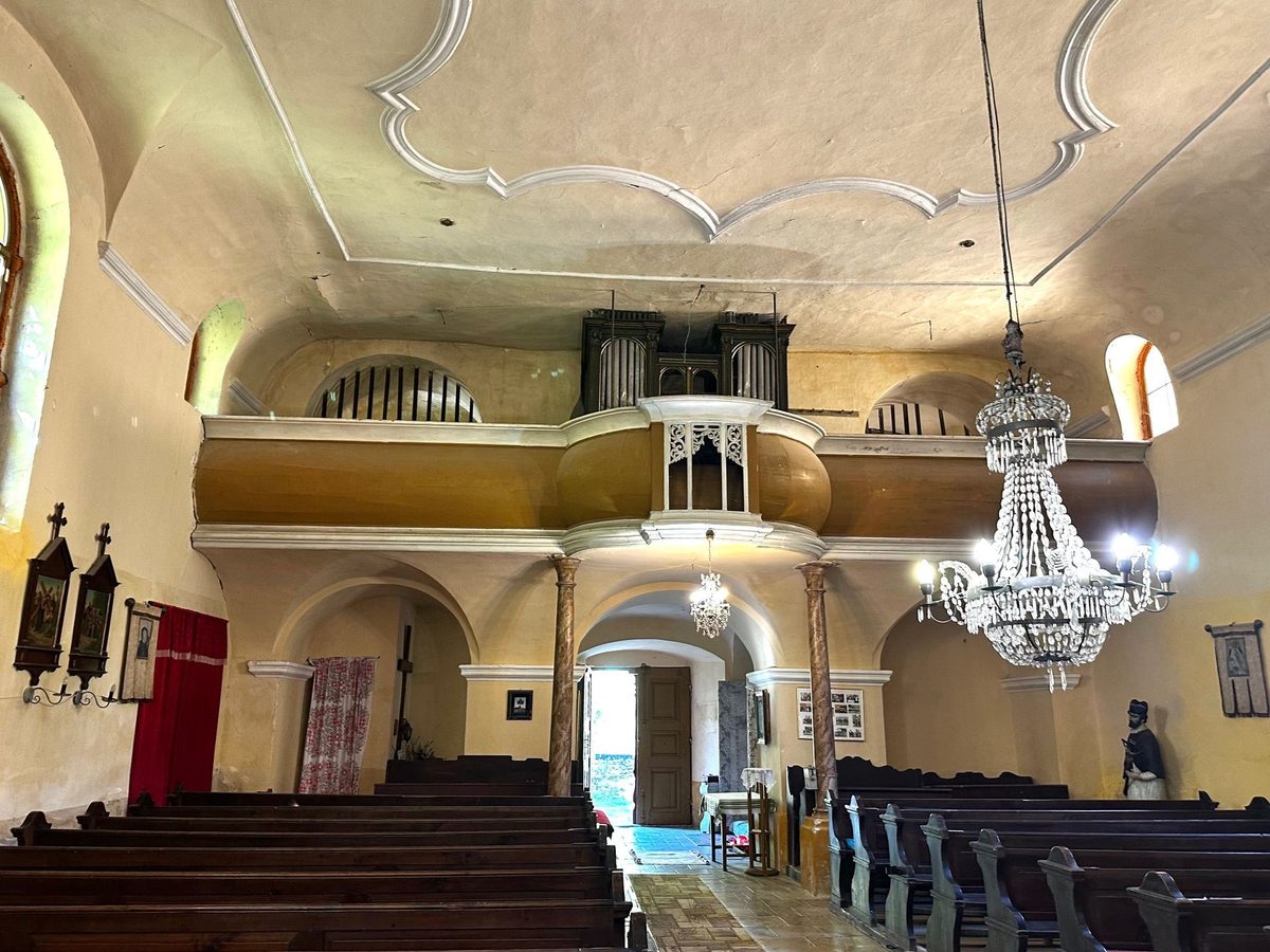 Balconul cu orgă de la intrarea în biserica catolică, cu candelabrul de cristal atârnat sub boltă