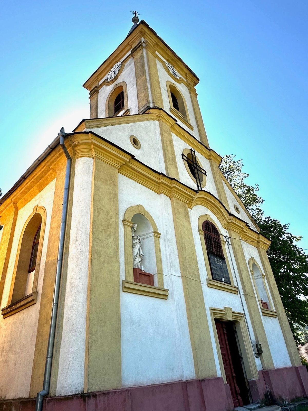 Fațada bisericii romano-catolice din Sasca Montană, cu turnul înalt și statuia din nișa de deasupra intrării