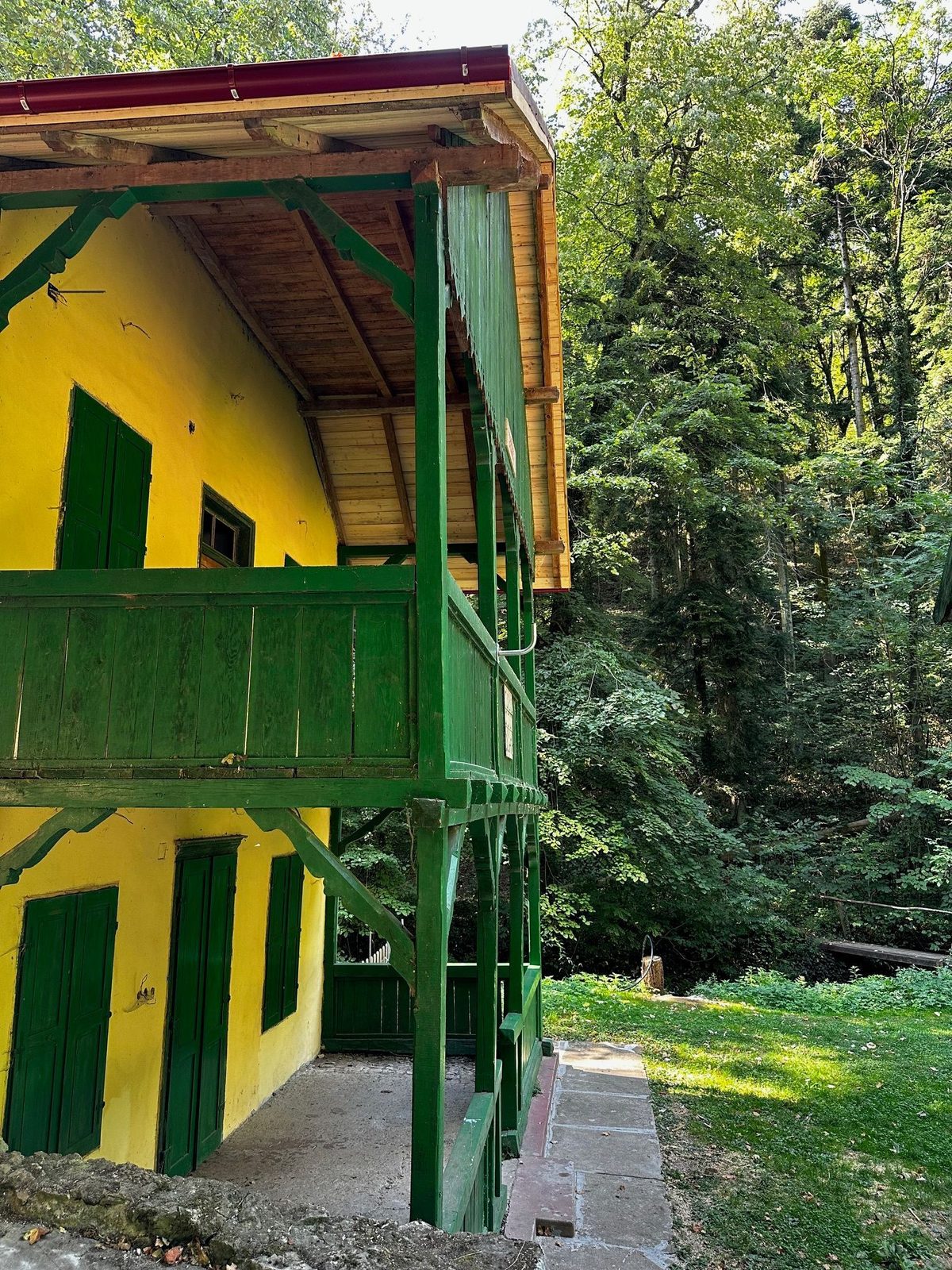 Colțul cabanei Șușara văzut de jos, cu stâlpii verzi ai balconului și streașina de scânduri nouă peste peretele galben