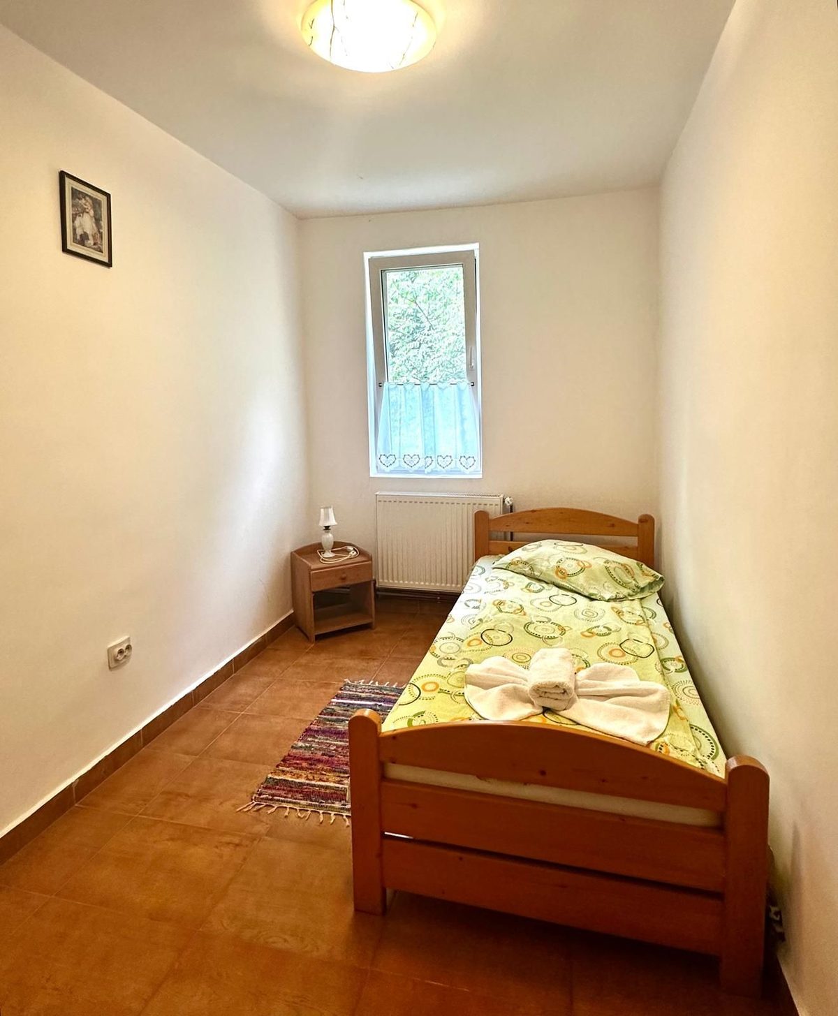 Cameră cu un singur pat, pardoseală de gresie terracotta și covor țesut pe jos