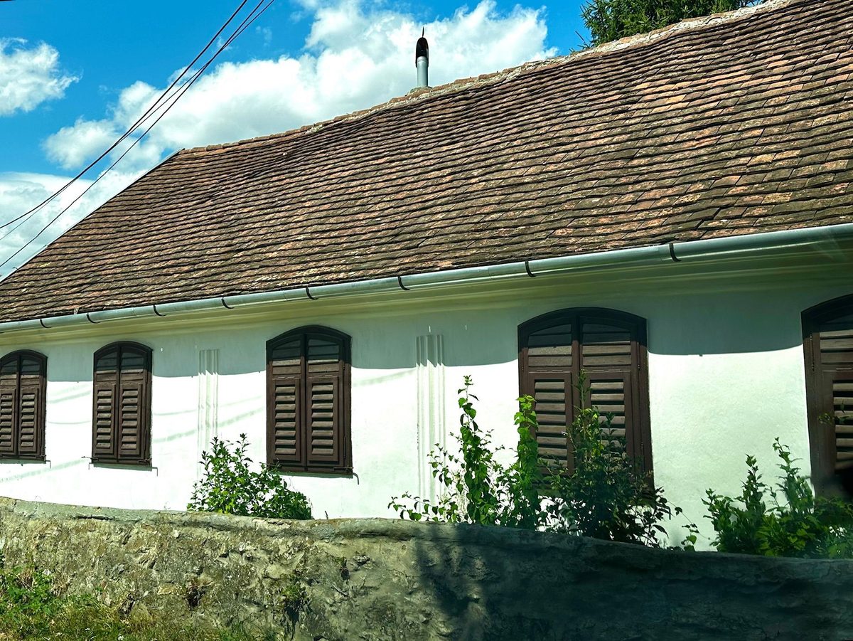 Casă lungă, albă, cu șase ferestre cu obloane maro, întinsă de-a lungul uliței din Cartierul Vărat