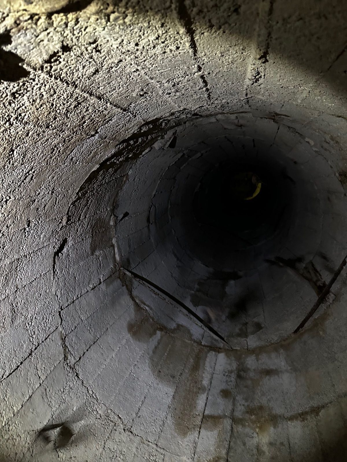 Gura rotundă a unei nișe săpate în peretele de beton al depozitului, cu tencuiala crăpată în jur