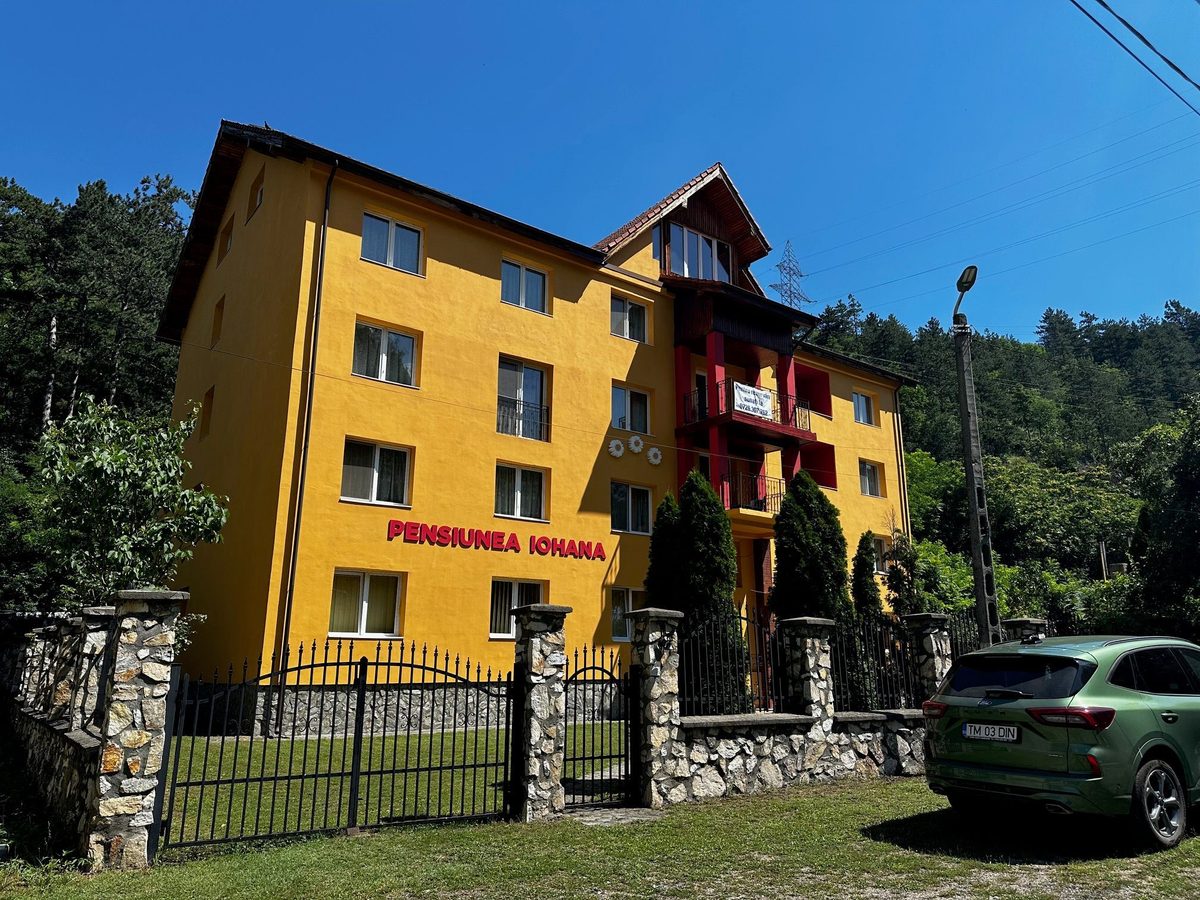Pensiunea Iohana văzută dinspre latura dinspre deal, cu balcoanele roșii și mansarda de lemn