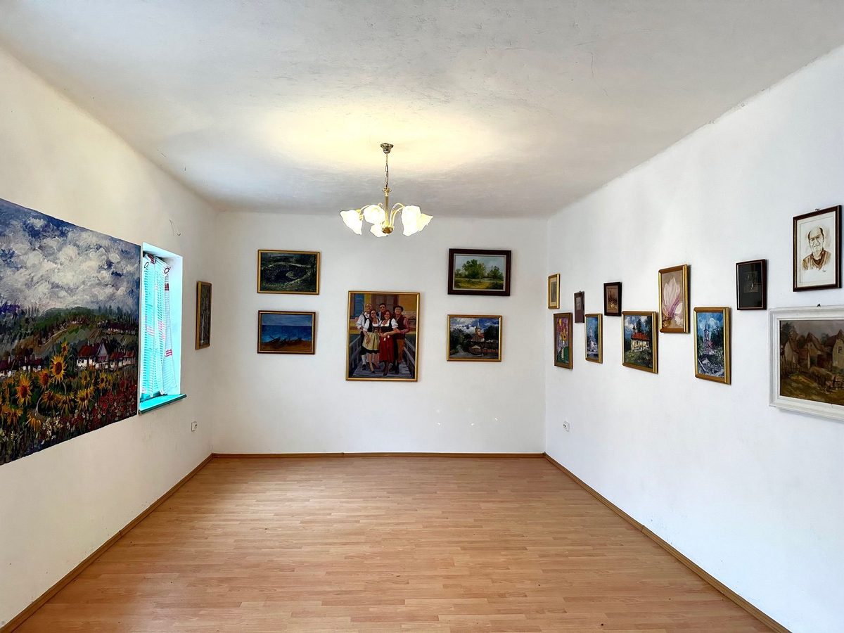 Sala lungă a galeriei, cu parchet gol și tablouri înșirate pe amândoi pereții, printre care o pânză mare cu un lan de floarea-soarelui lângă fereastră