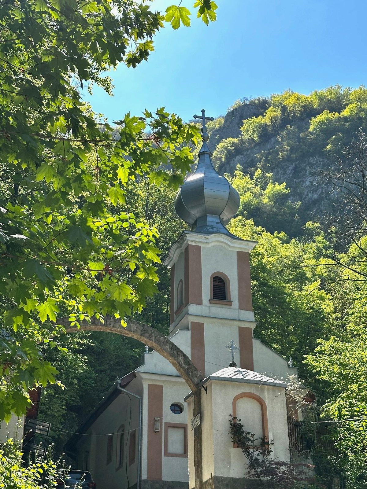 Turnul bisericii Mănăstirii Călugăra zărit printre frunzele de paltin, cu peretele de calcar în spate