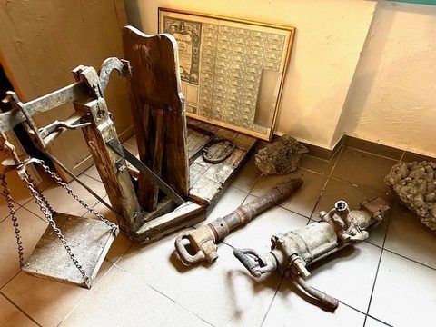 Unelte de perforat și târnăcoape rezemate de peretele muzeului, lângă un tablou cu un tabel