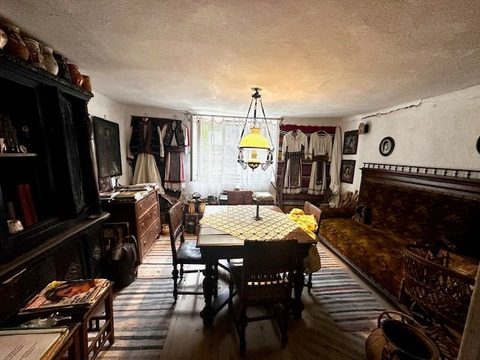 Camera de zi a muzeului, cu masa de lemn sub lampa cu abajur galben, costume populare atârnate pe perete și covor țesut pe jos