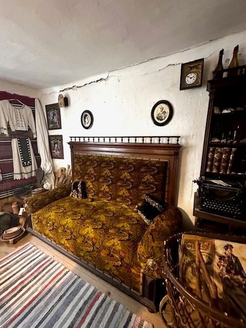 Cămăși și fuste de sărbătoare atârnate pe perete lângă canapeaua de salon, cu ceasul cu pendul deasupra