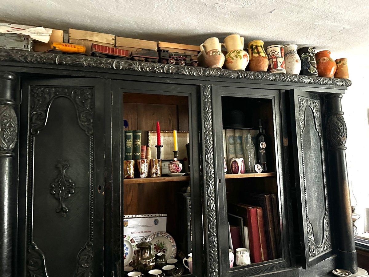 Dulap negru sculptat, cu ulcioare pictate și un trenuleț de tablă așezate deasupra