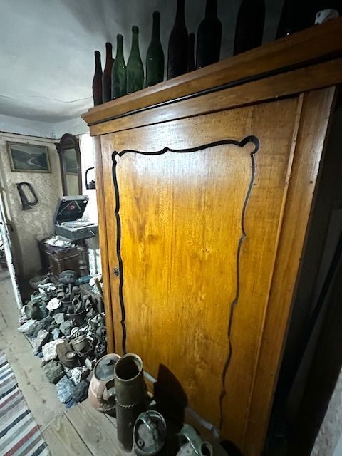Grămadă de lămpi de miner de alamă, adunate pe podea lângă un dulap de nuc, cu sticle vechi înșirate deasupra