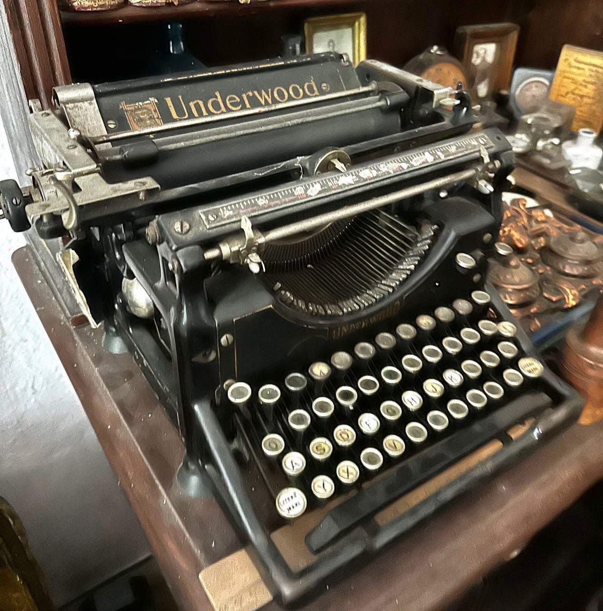 Mașină de scris Underwood cu taste de sidef, pe o masă încărcată cu rame și obiecte de alamă