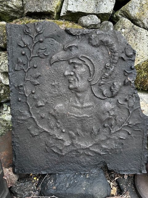 Placă de fontă turnată cu portretul unui bărbat cu coif, într-o cunună de lauri, sprijinită de zidul de piatră al curții