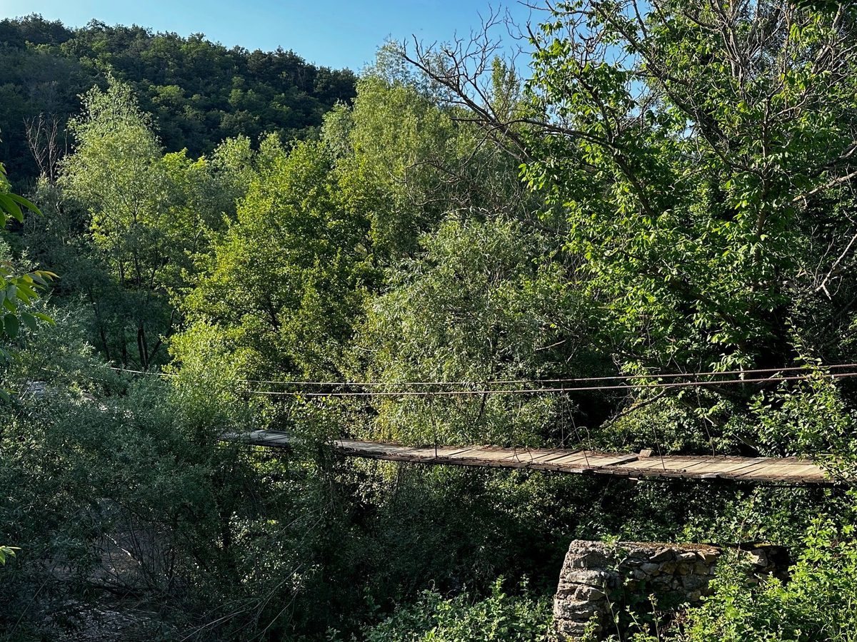 Puntea suspendată peste Nera, la capătul satului Sasca Română, cu dealurile împădurite în spate
