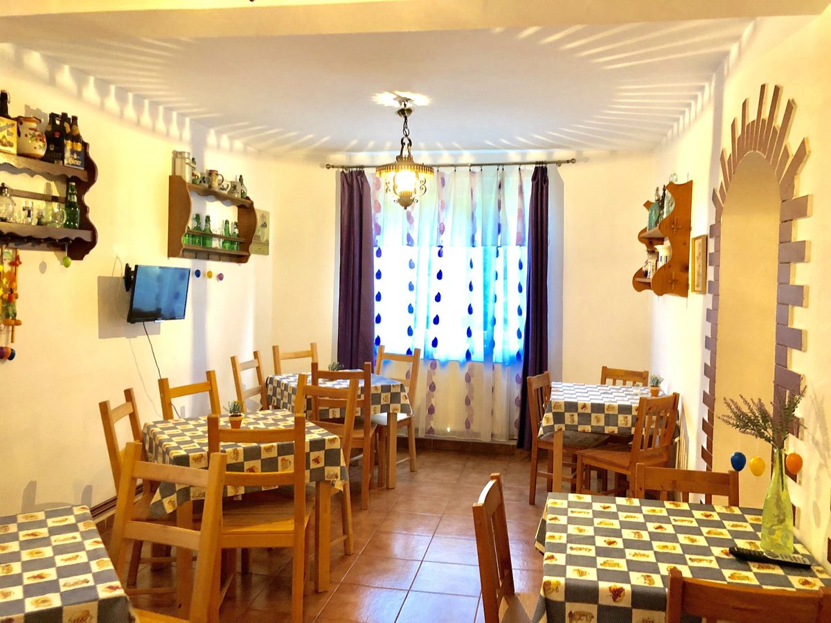 Sala de mese cu mese lungi așezate pentru grup, cu ferestrele spre deal