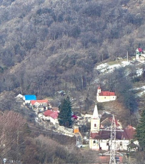 Turla albă a bisericii ieșind dintre casele Sascăi, privită de sus, de pe versantul din față