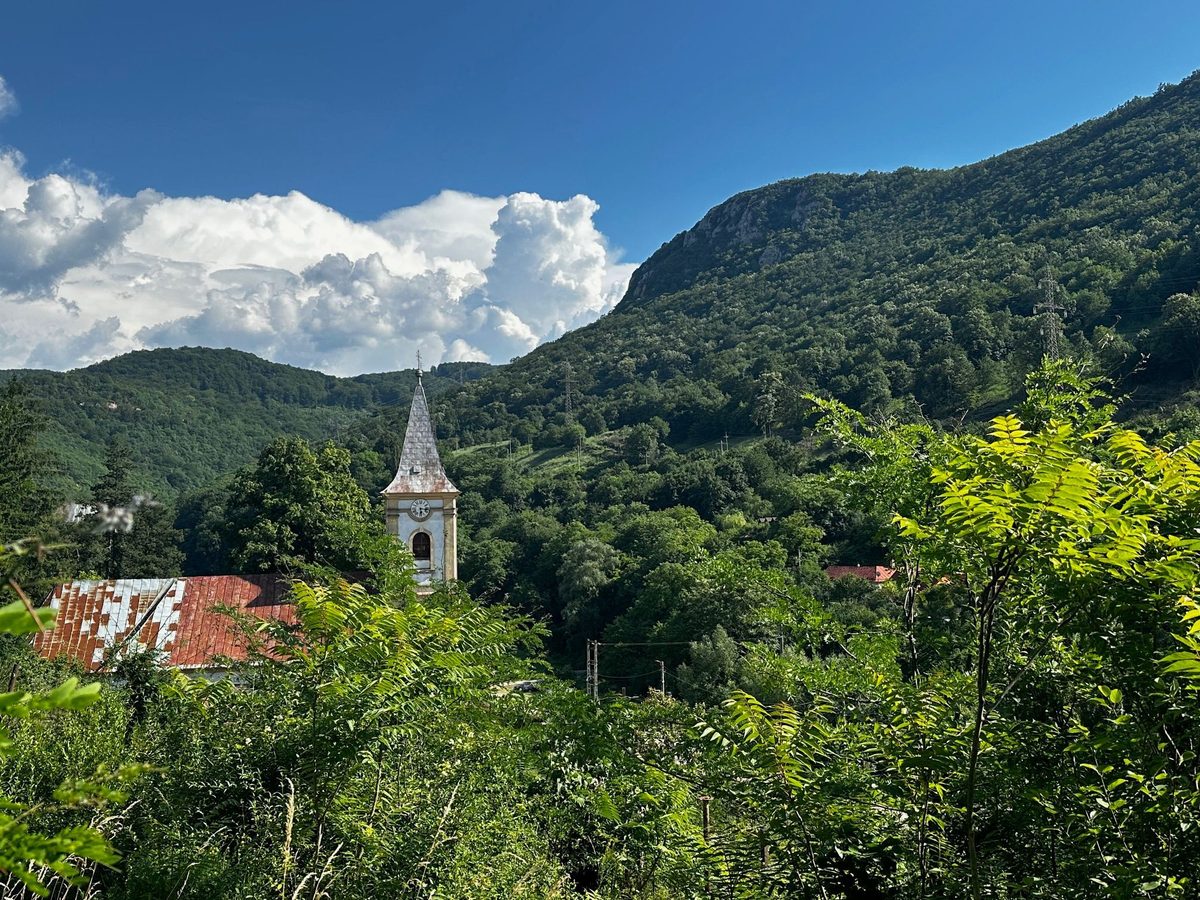 Turla bisericii și acoperișurile satului sub un cer de vară cu nori grei, cu muntele închizând valea în spate