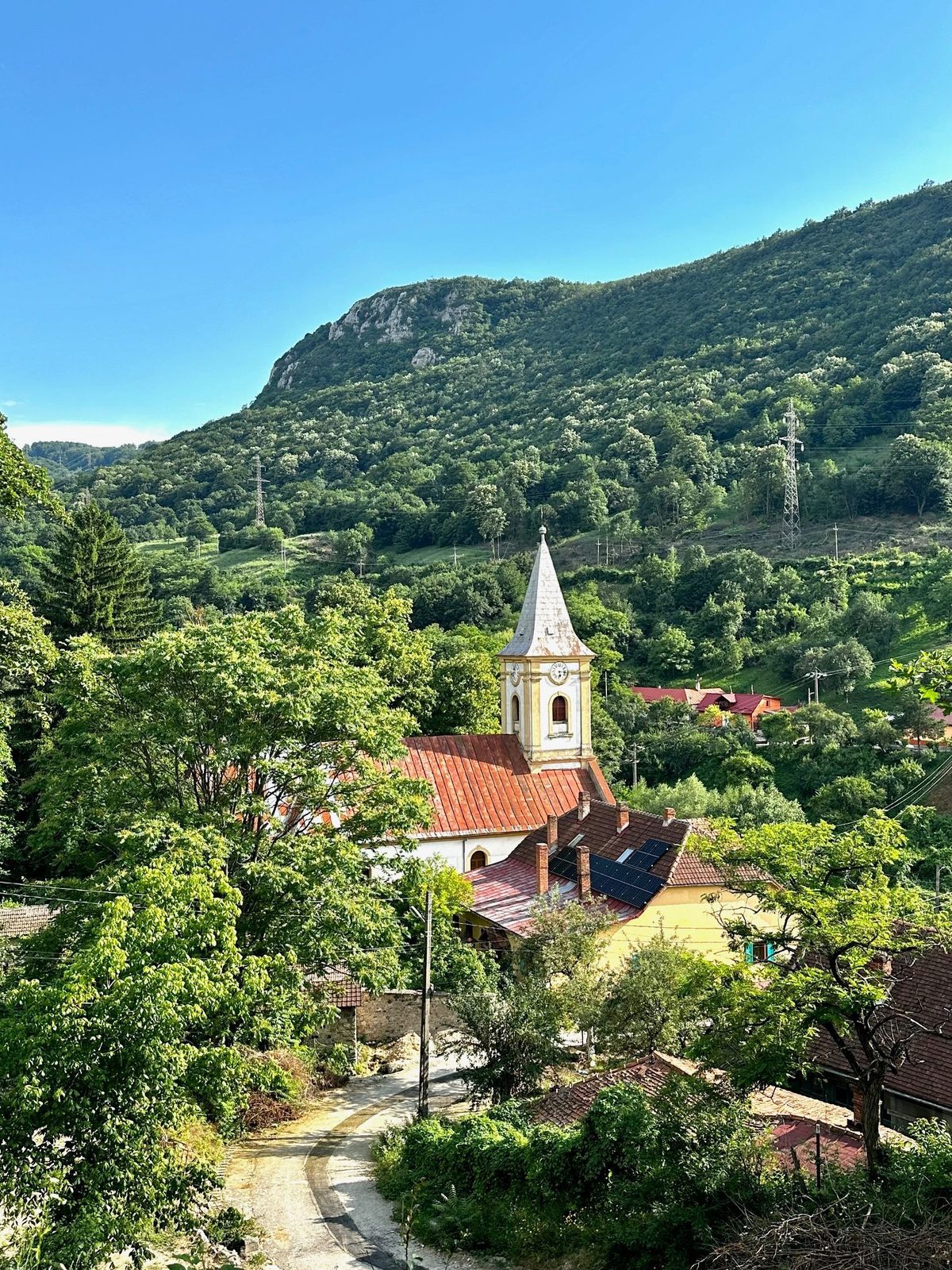 Sasca Montană dimineața, cu turla bisericii ieșind dintre acoperișurile de olană și creasta calcaroasă deasupra satului