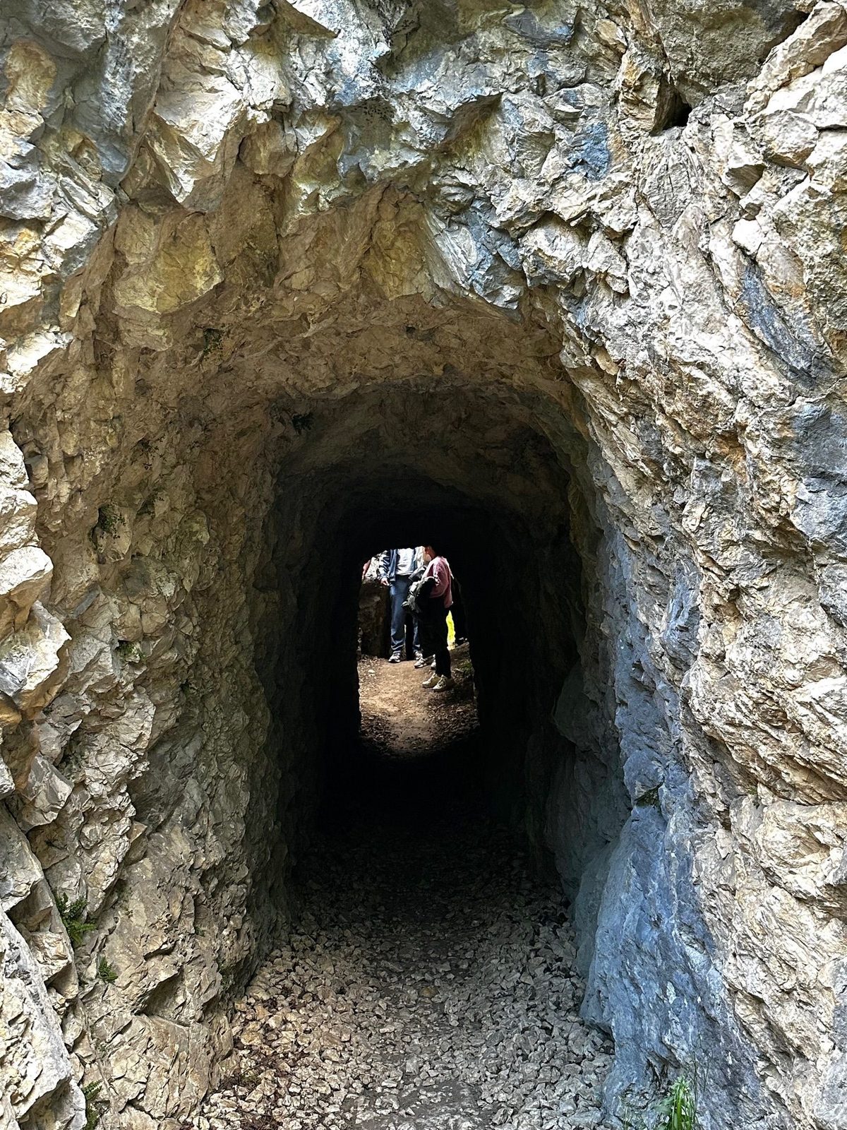 Interiorul unui tunel de pe traseu, cu urmele daltei în pereți și un grup de drumeți conturați în lumina de la celălalt capăt